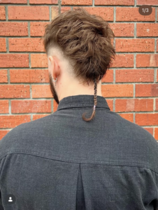 Close-up back view of a men’s tailored mullet featuring a distinct long, thin rat tail at the nape with sharp, precision-cut sides and textured crown, styled at Assort Osaka.